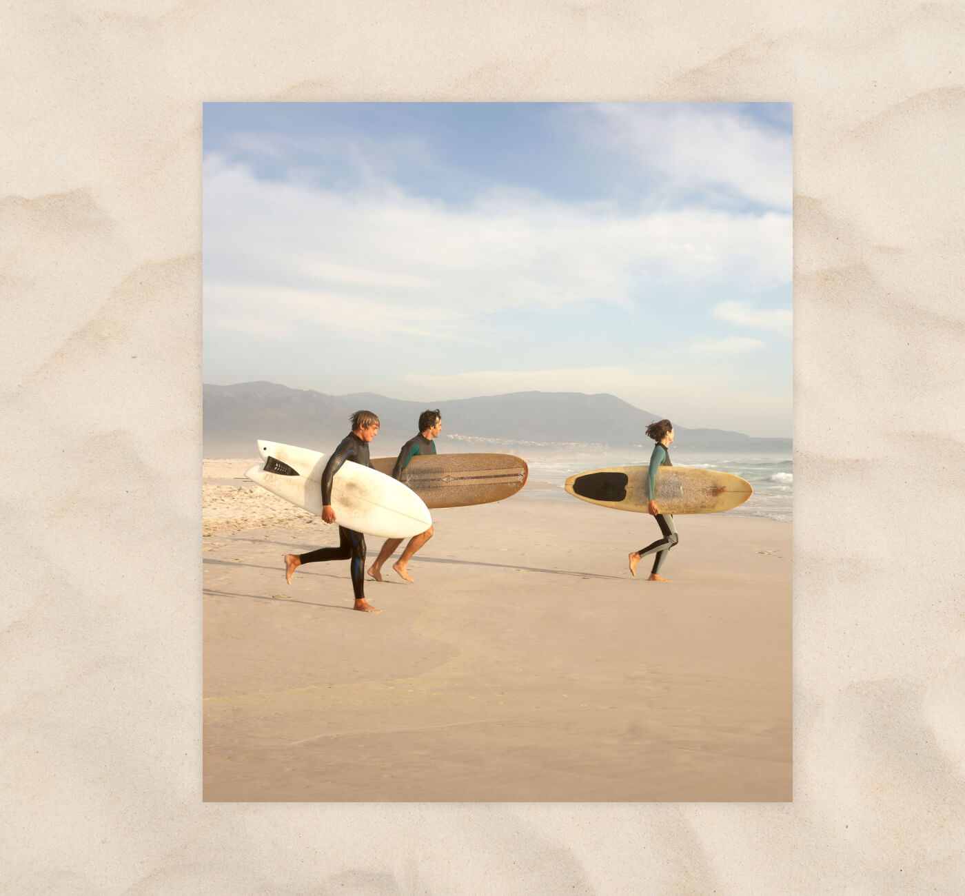 three surfers running on beach